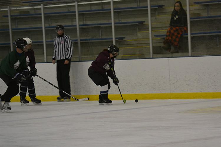 This image shows a female getting the puck along the boards at adult hockey.
