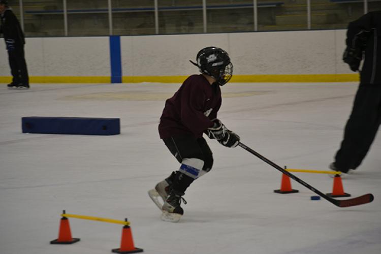 This image shows a boy doing a cone drill at youth hockey skills training.