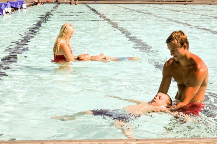 This image shows two lifeguards teaching kids to swim.