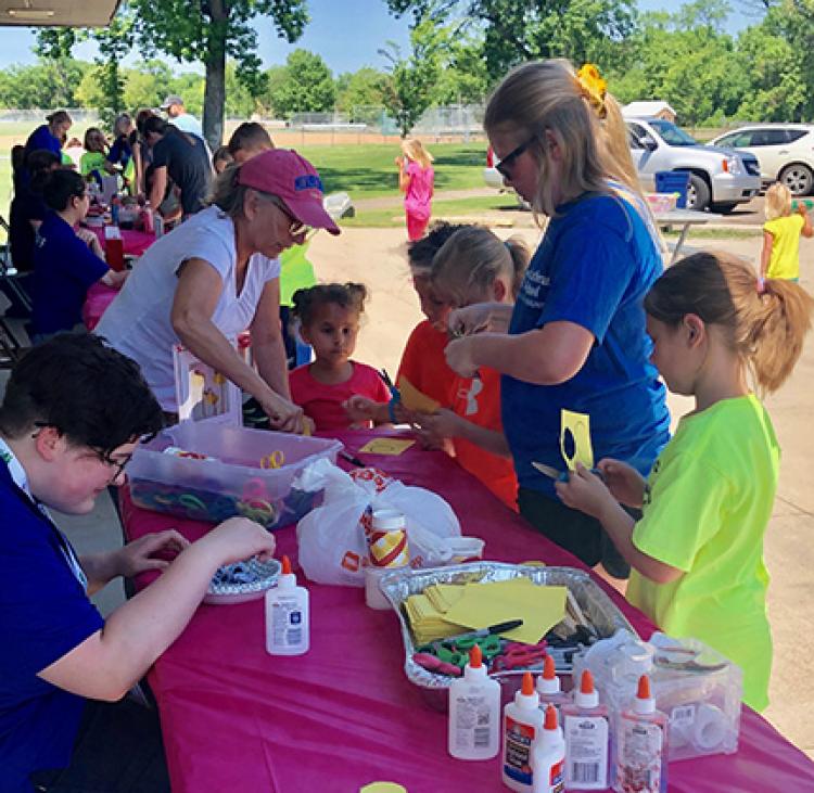 This image shows a table outdoors with kids all around learning how to make a craft at Park It.