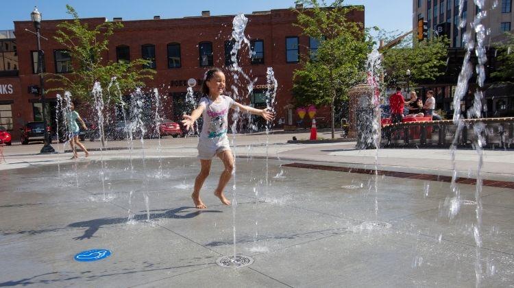 This image shows a young girl playing in The Square Spouts, an interactive water feature at Broadway Square.