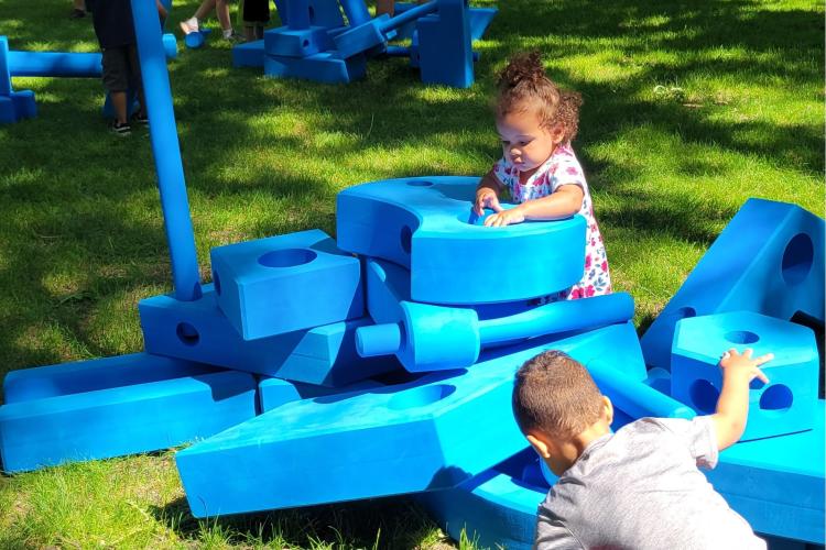 Toddler playing with large blue foam stacking blocks in island park