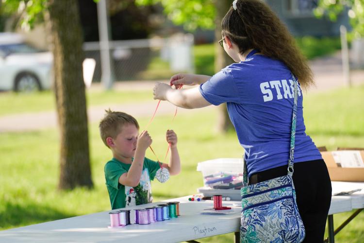 Kid making a medal for his award at craft table with staff member assisting