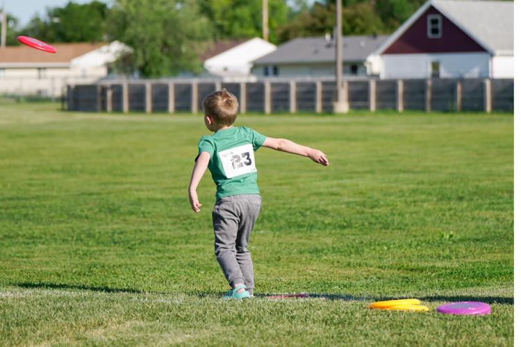 kid in grass field with participant number bib on throwing a frisbee