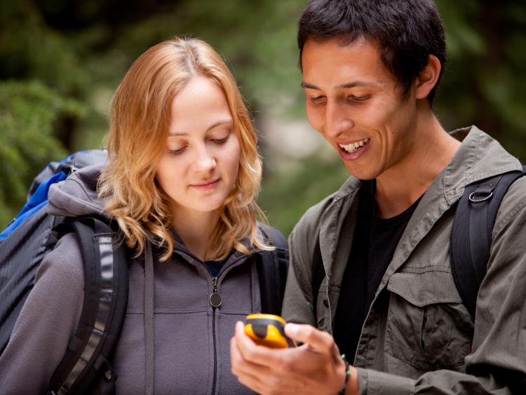 A woman and man looking at a GPD device in backpacks in park