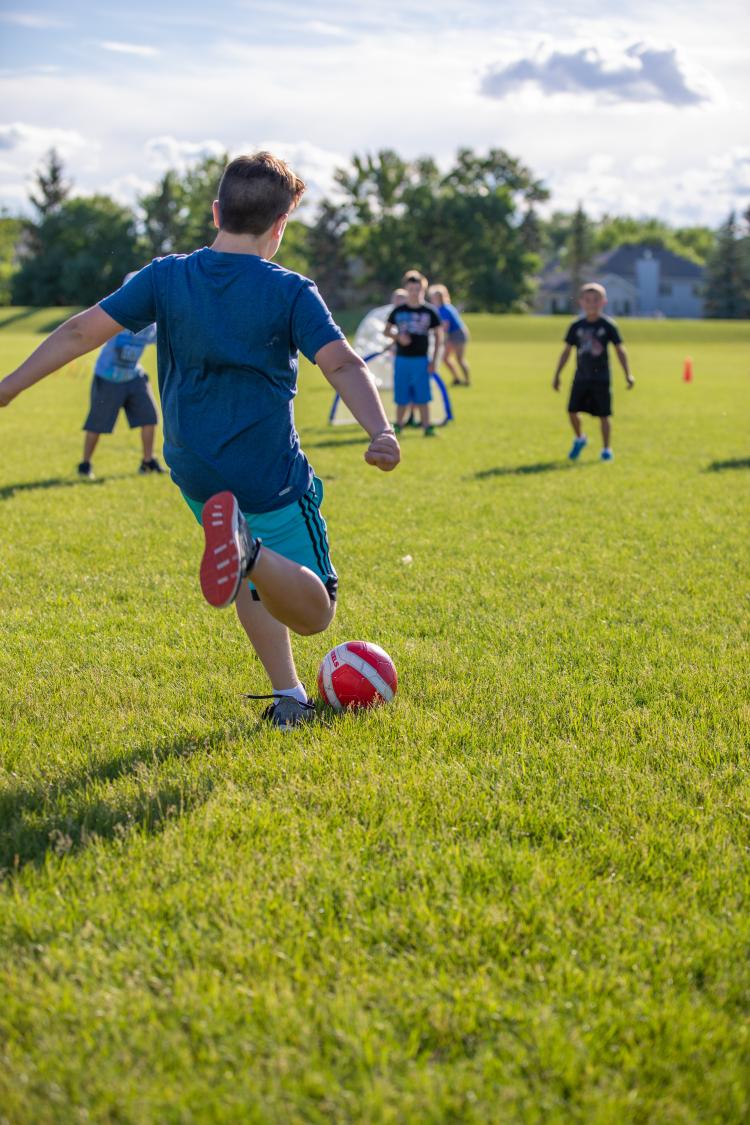 Boy kicking soccer ball Boy kicking soccer ball in park into 3 boys waiting