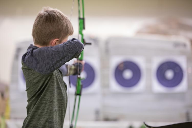 Back of young boy lining up bow and arrow to shoot at target