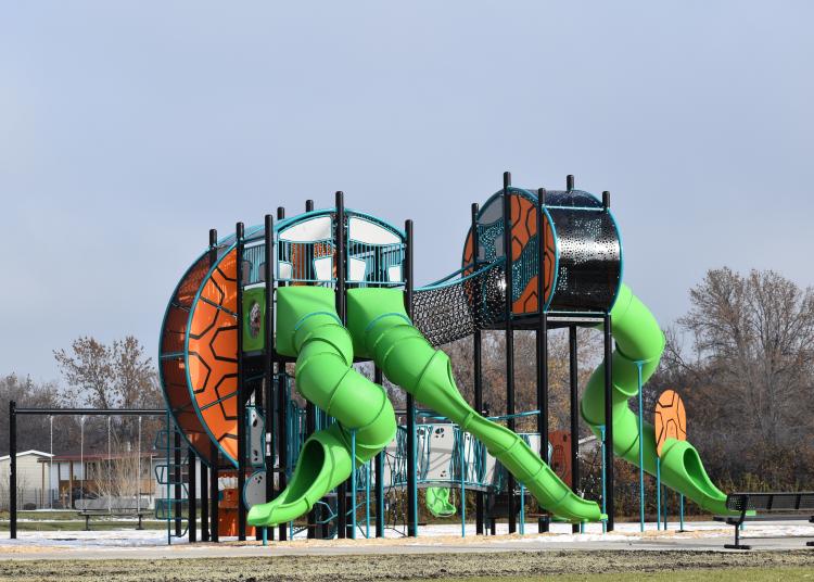 Village West Playground 2-Story Playground with 3 green slides, a climbing structure, a swing set and a rope bridge