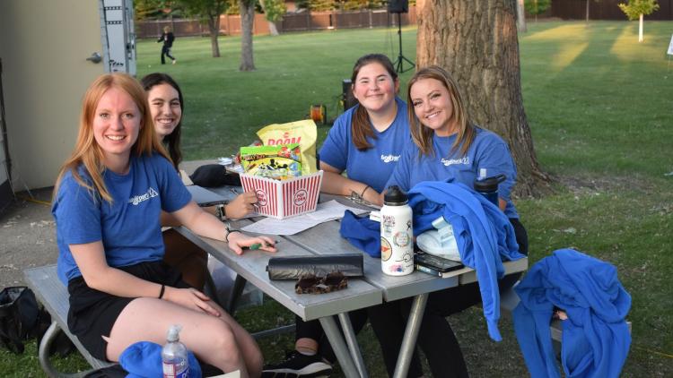 group of 4 ladies stilling at a picnic table, all wearing a blue Fargo Parks staff t-shirt.  This picture is at Rheault Farm of the events intern and staff.