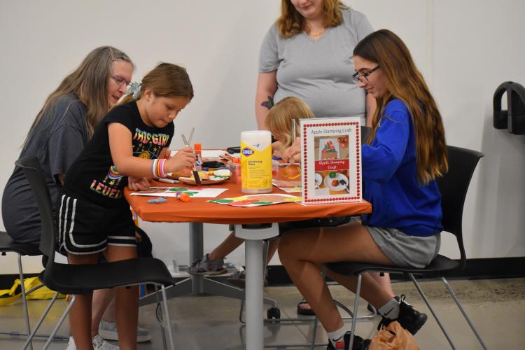 Three young children and their moms sitting at a table working on a craft project.