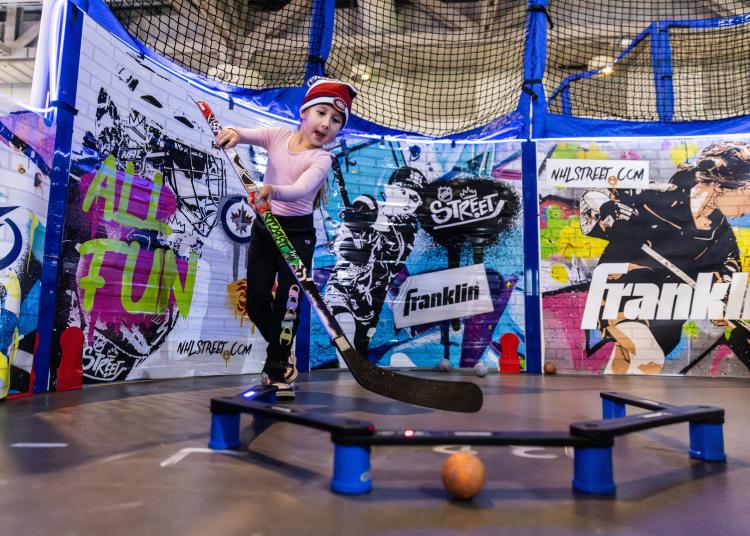 NHL STREET Child practicing stick handling with colorful boards behind her on concrete floor