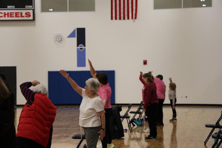 adults 55+ standing in gym with chair next to each stretching for the SAIL program