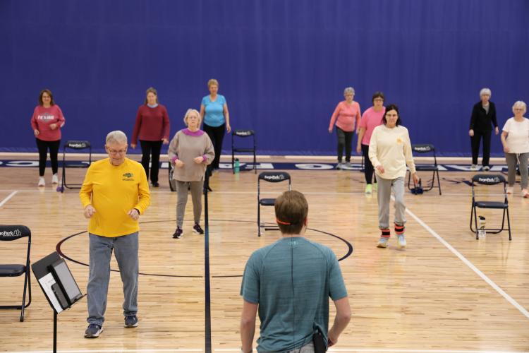 adults 55+ standing in gym with chair next to each stretching for the SAIL program