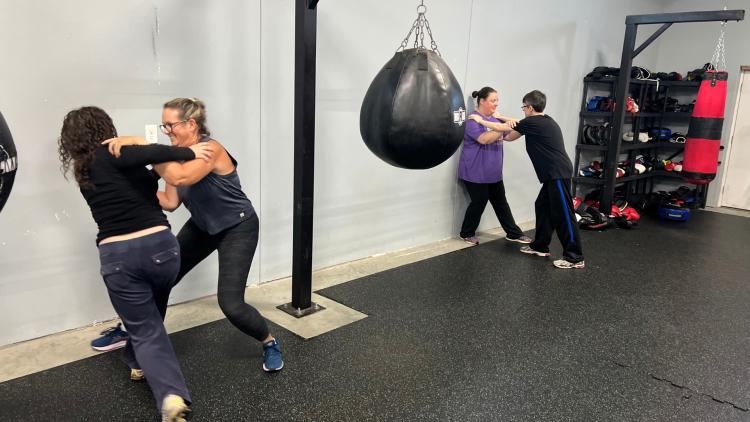 Participants pair up to practice self-defense techniques in a gym setting.