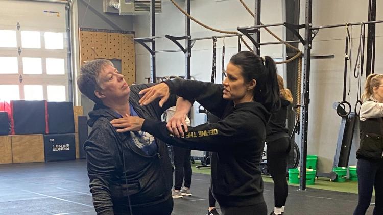 An instructor demonstrates a self-defense technique with a participant in a training space.