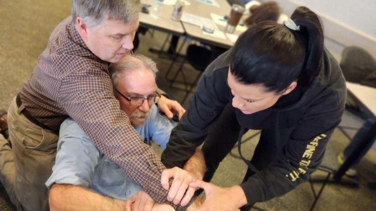 An instructor guides participants through a hands-on self-defense technique during a class.