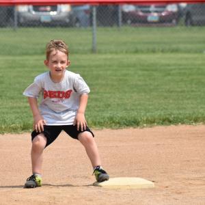 Young boy leading off the base on a baseball field outside on a beautiful day. 