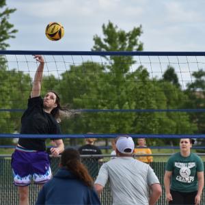 Outdoor Sand Volleyball Match - Man jumping up to spike a volleyball over the net to a set of people waiting