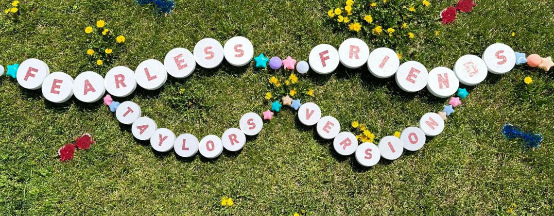 large friendship bracelet on grass that says "Fearless Friends Taylor's Version" 