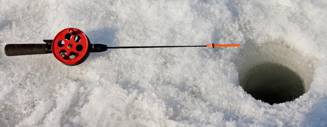 Photo of an ice fishing pole next to an ice fishing hole in the ice