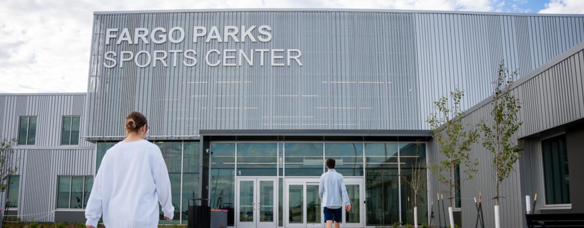 Two people walking into the main entrance of the Fargo Parks Sports Center