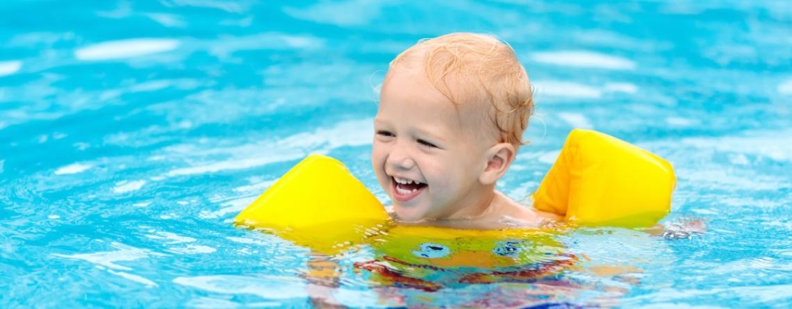 Blonde white child in a yellow floaty vest playing in a pool 