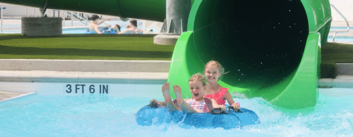 two young girls coming out of the green tube slide at Island Park Pool 