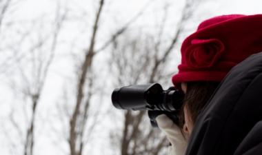 woman in red hat looking through binoculars in snowy forest