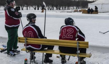 three men sitting on bench outside pond hockey rink