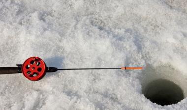 Photo of an ice fishing pole next to an ice fishing hole in the ice