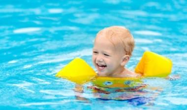 Blonde white child in a yellow floaty vest playing in a pool 