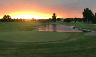 sun setting over putting green with red flag and water hazard on right side