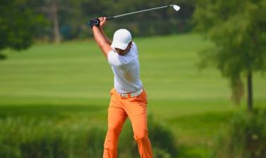 A young man golfing on a green course wearing orange pants and a white shirt and hat