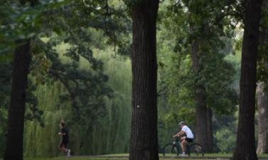 Person jogging and another person riding a bicycle along a paved trail through a wooded Fargo park.