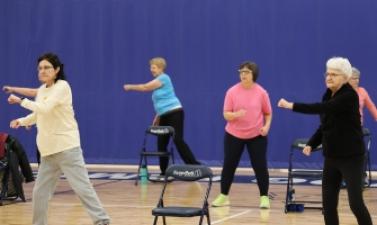 6 women in a gym doing light exercise. 