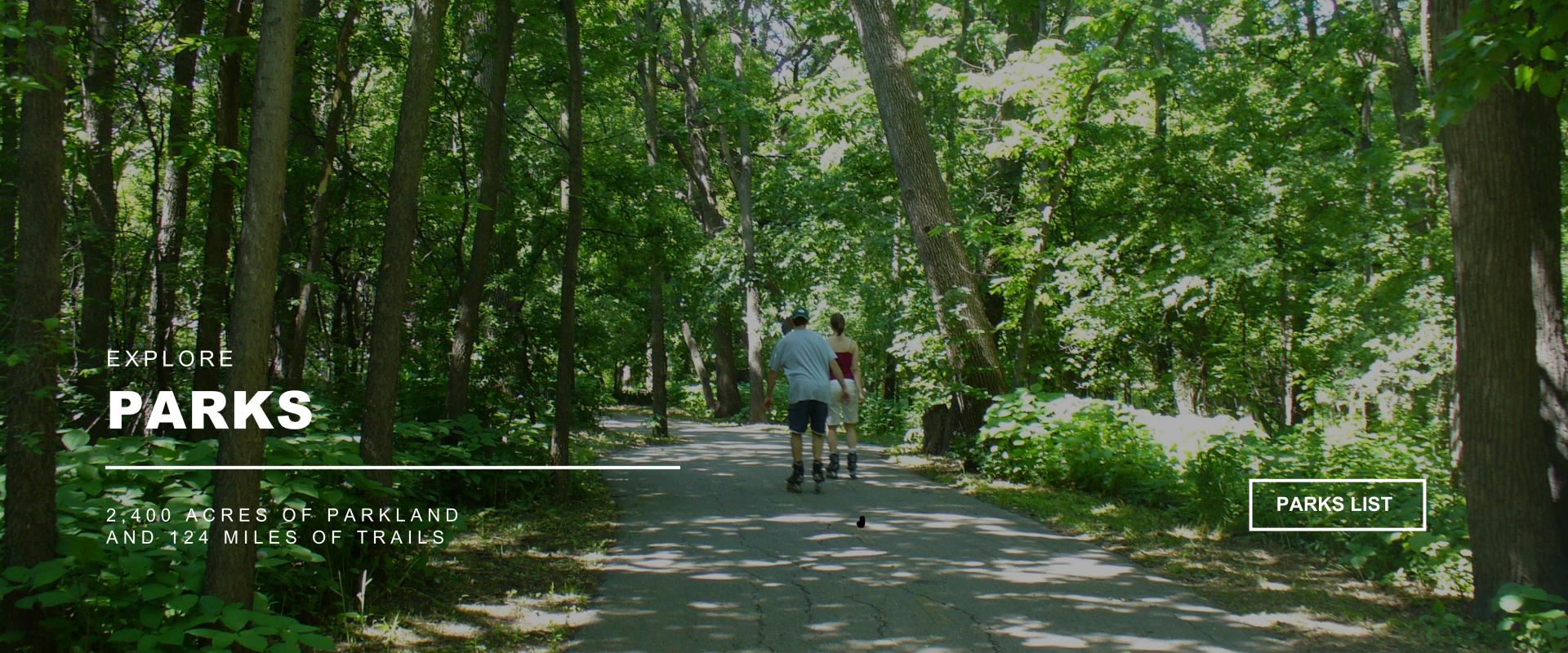 Explore PARKS - 2,400 acres of parkland and 124 miles of trails  - image of two people rollerblading on a path through trees