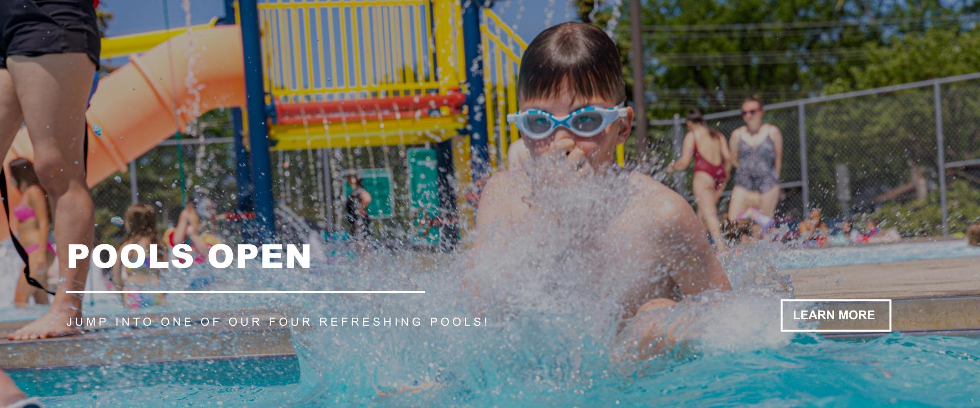 POOLS OPEN - Jump into one of our FOUR refreshing pools! - boy with goggles doing a canon ball into a pool with a slide and people in the background - Learn More button