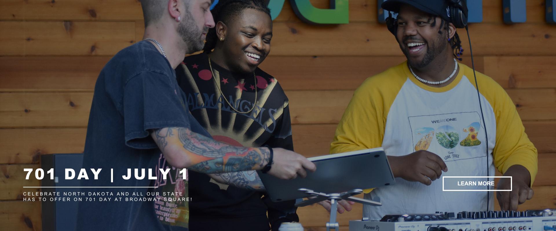 Three men smiling and talking while setting up DJ equipment at an outdoor event. Text overlay reads “701 Day | July 1 – Celebrate North Dakota and all our state has to offer at 701 Day at Broadway Square.