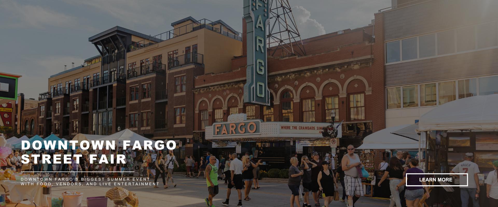 Crowds walking through downtown Fargo during a summer street fair with tents, vendors, and the historic Fargo Theatre sign in view. Text overlay reads “Downtown Fargo Street Fair – Downtown Fargo’s biggest summer event with food, vendors, and live entertainment.