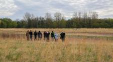 Photo shows people standing in field looking for birds.