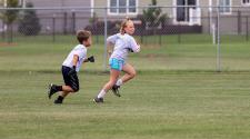 This image shows a girl running with the football and a boy following her at the youth football program.