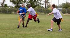 This image shows a boy carrying a football and running from two boys at the youth football program.