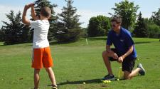 This image shows the coach helping a boy during youth golf lessons.