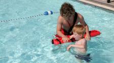Photo shows lifeguard helping boy in pool at Water Safety Day.