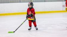 This image shows a boy skating indoors with a hockey stick. 