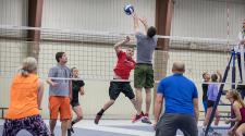 This image shows adults playing a coed volleyball game. 