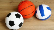 This image shows a soccer ball, basketball and volleyball sitting on the court.