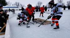 This image shows three players battling for the puck during youth pond hockey.
