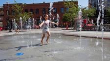 This image shows a young girl playing in The Square Spouts, an interactive water feature at Broadway Square.