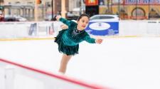 This image shows an ice skater performing on SCHEELS Skating Rink at Broadway Square.